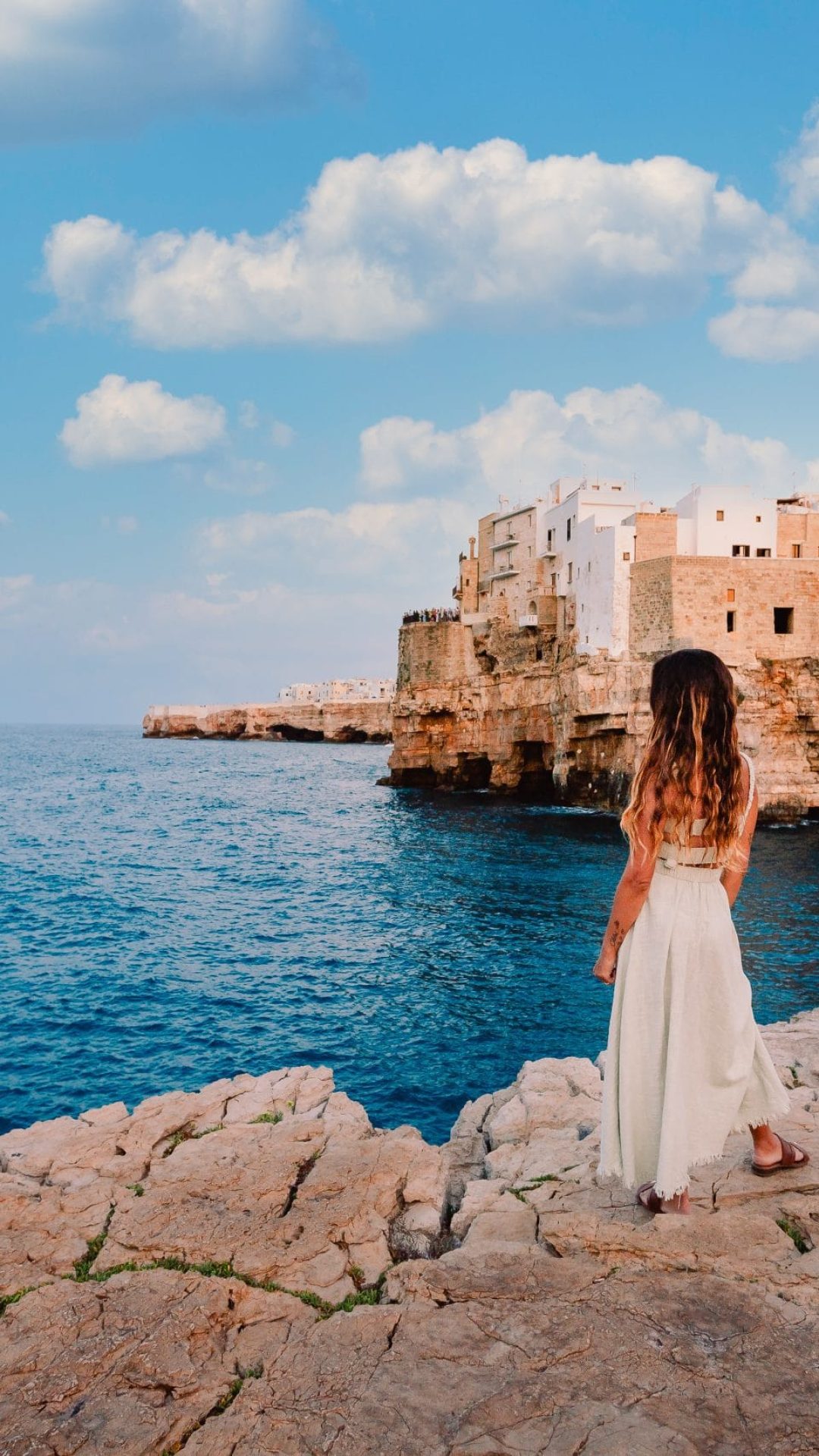 Young girl in front of the village of Polignano a Mare, sky with white clouds Polignano a Mare, Italy - August 2021: Young girl in front of the village of Polignano a Mare, sky with white clouds